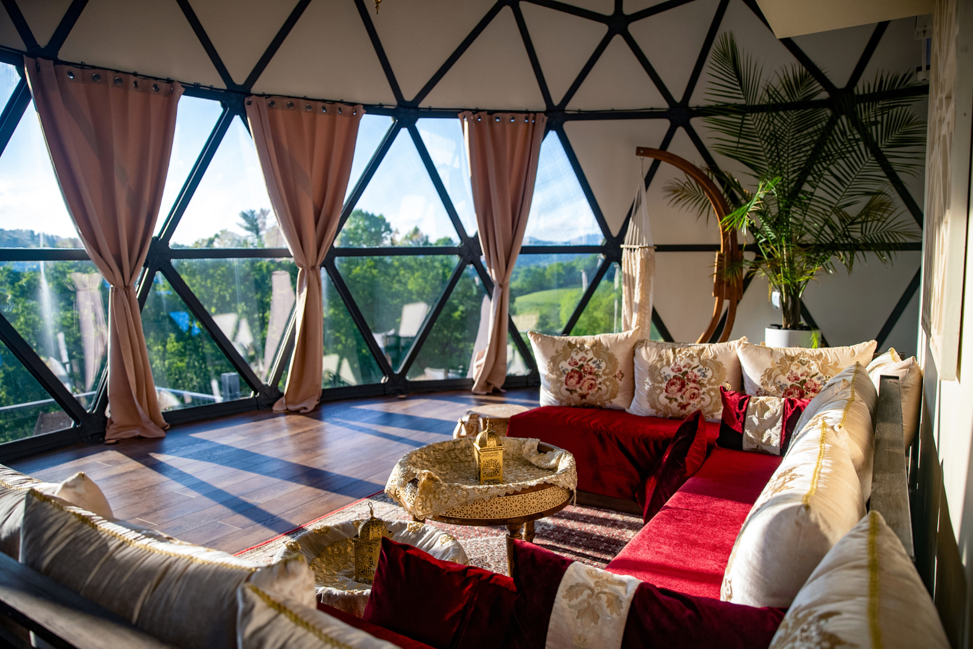 Geodesic dome lounge with pink curtains, red velvet seating, and Moroccan brass tables overlooking mountain views