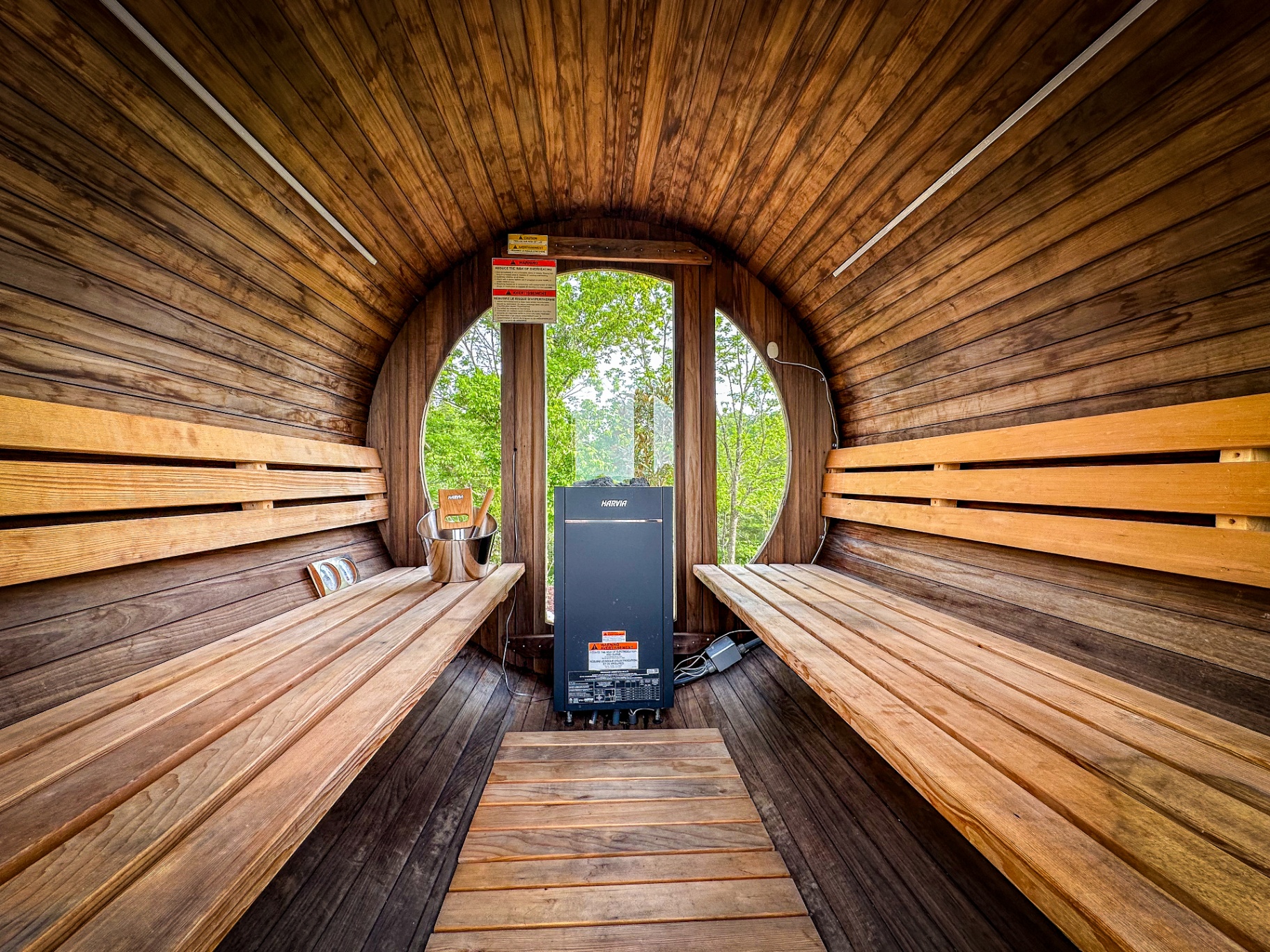 Wooden barrel sauna interior with round windows overlooking the forest at Munaya