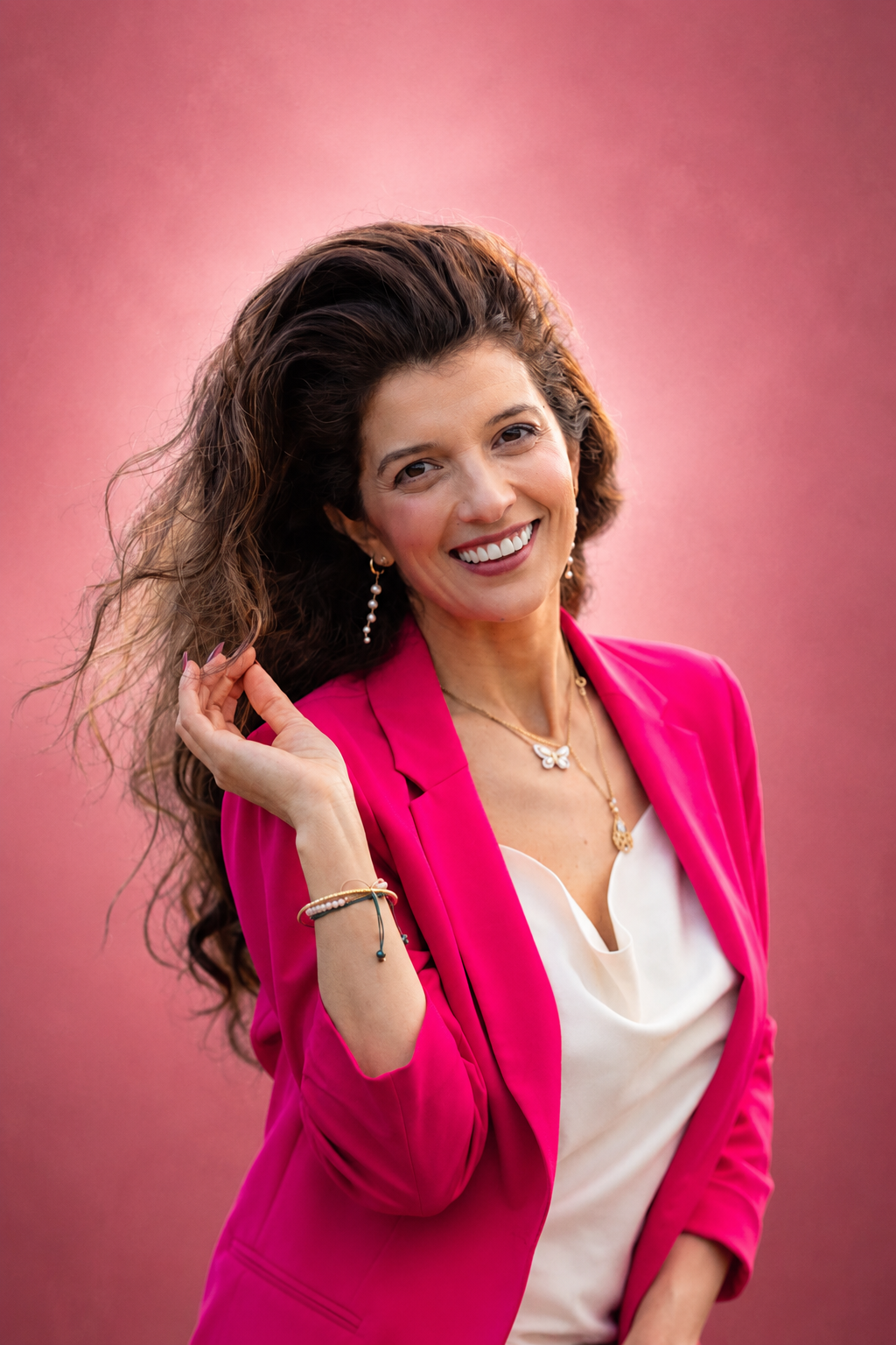 Saloua smiling in a fuchsia blazer against a rose backdrop